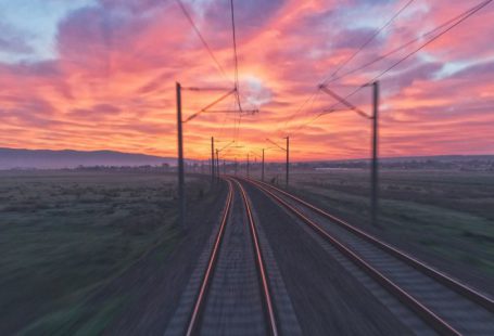 Train - empty train tracks near green grass during sunset