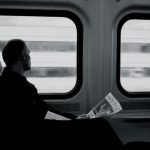 Train - man inside train looking on window while holding newspaper grayscale photography