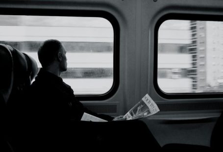 Train - man inside train looking on window while holding newspaper grayscale photography