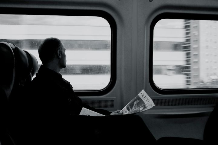 Train - man inside train looking on window while holding newspaper grayscale photography