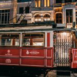 Train History - Old fashioned tramway riding on rails along paved street with buildings in city