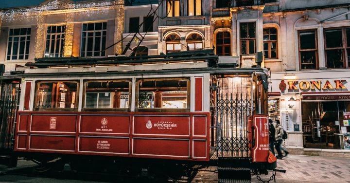 Train History - Old fashioned tramway riding on rails along paved street with buildings in city