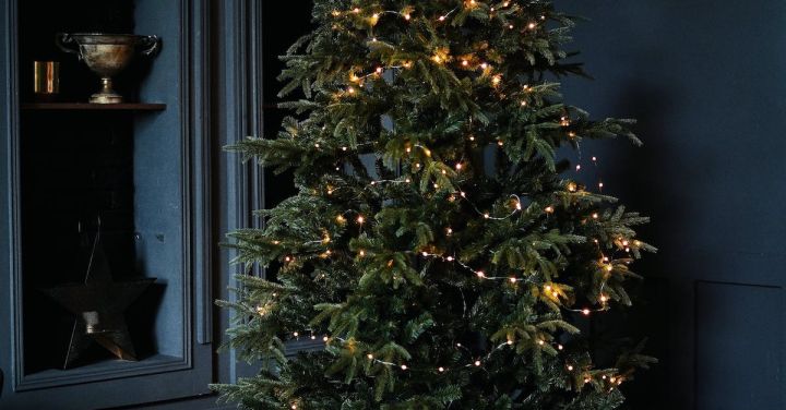 Holiday Seasons - Tall green Christmas tree decorated with small glowing garlands and surrounded by shelves and bunch of boxes with gifts in dark room