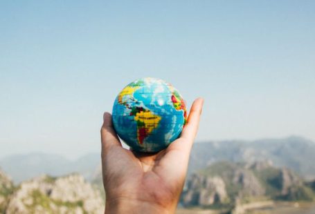 Travel Insurance - Person Holding World Globe Facing Mountain