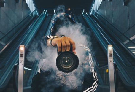 Photography - Man Holding Camera While Squating With Smoke on Face Inside Building