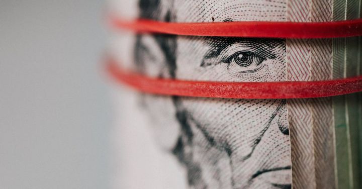 Budget Tips - Closeup of rolled United States five dollar bills tightened with red rubber band